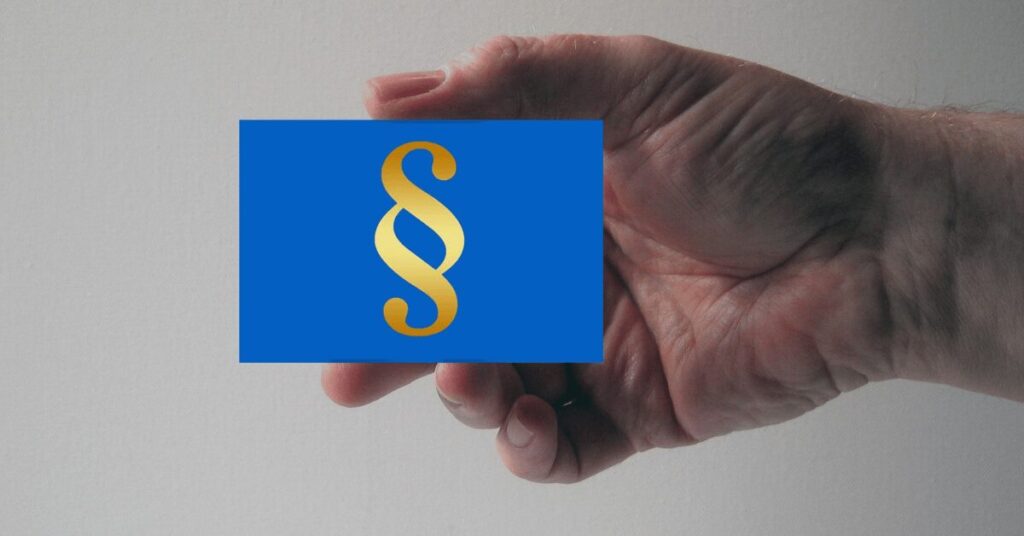 Hand hält eine blaue Karte mit goldener Paragraphen-Symbol (§), symbolisch für Recht und Gesetz