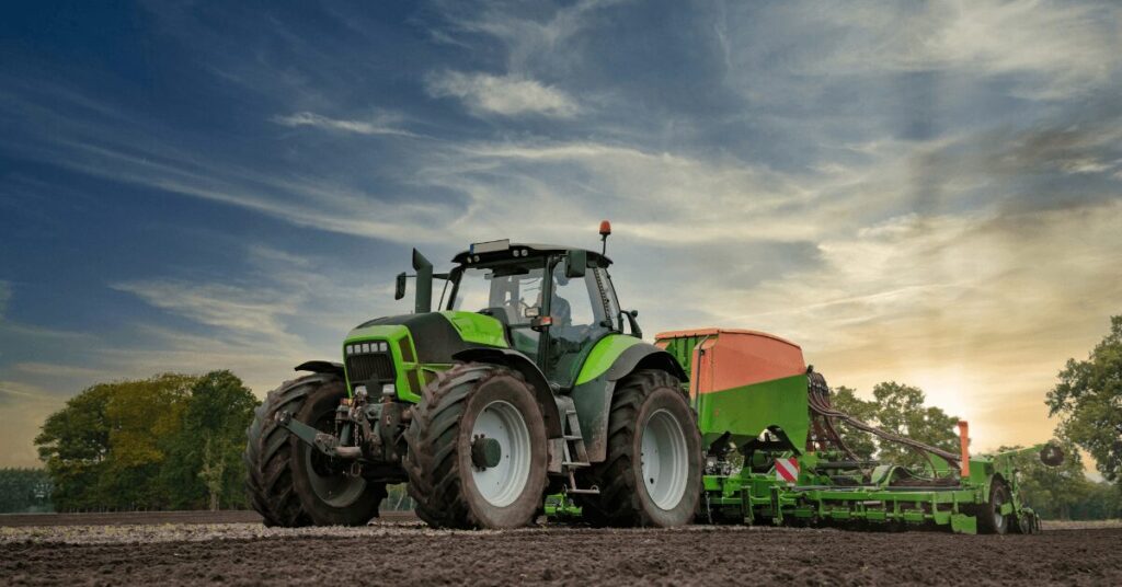 Moderner grüner Traktor bei der Winterraps-Aussaat auf einem Acker bei Sonnenuntergang